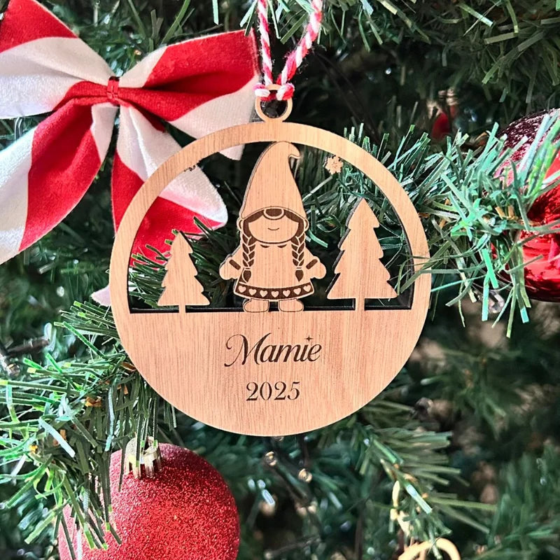 Suspension en bois personnalisée Mamie 2025 avec lutin et sapins gravés, accrochée dans un sapin de Noël décoré.
